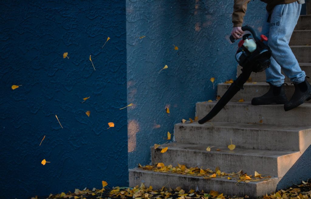 Man blowing leaves from stairs—electric leaf blower and gas leaf blower.